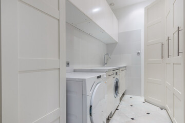 The laundry room shows a washing machine and dryer next to white cabinets and a sink. The space is clean and organized with tiled flooring