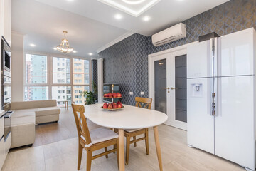 A dining table with red apples sits in a kitchen with grey walls and modern furniture in a high-rise apartment. Large windows let in natural light, creating an inviting space