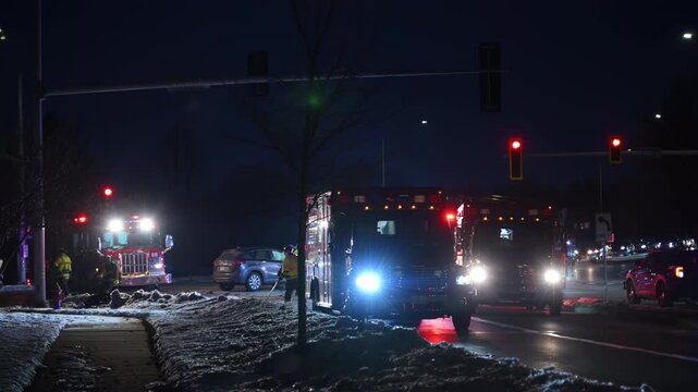 Nighttime scene of multiple emergency vehicles responding at an intersection with flashing lights. Police cars, fire trucks, ambulances, cars stopping at a red light