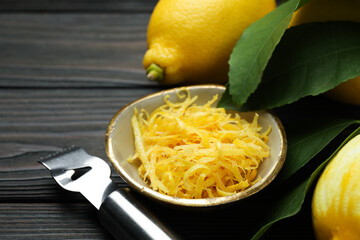 Lemon zest, fresh fruits and zester tool on wooden table, closeup