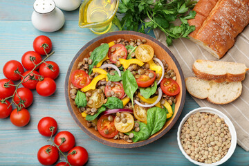 Tasty lentil salad, ingredients and bread on light blue wooden table, flat lay