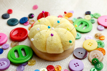 Yellow pincushion with pins and colorful buttons on light cloth, closeup