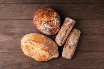 Different types of bread loaves on wooden table, flat lay