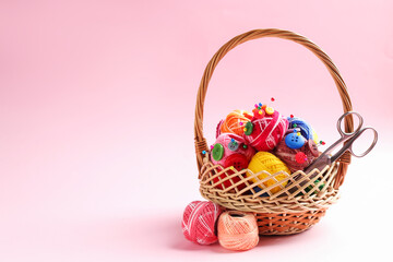 Bright yarns, pins, buttons, scissors and wicker basket on pink background, closeup. Space for text