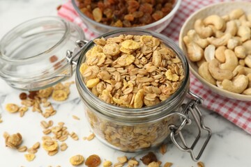 Tasty granola in glass jar on white marble table, closeup