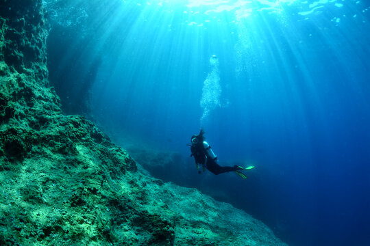 Silhouette of a scuba diver underwater, emphasizing human scale against the vast marine environment. Concept of exploration, isolation, and discovery.