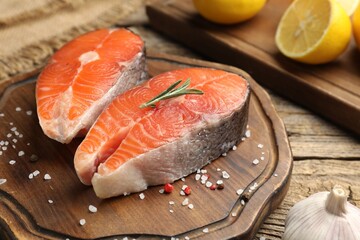 Pieces of fresh salmon fillet, salt, garlic, rosemary and lemon on wooden table, closeup