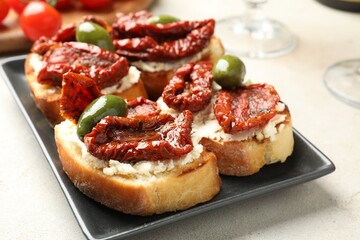 Delicious bruschettas with cream cheese, sun-dried tomatoes and green olives on gray table, closeup