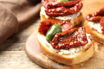 Delicious bruschettas with cream cheese, sun-dried tomatoes and green olives on wooden table, closeup