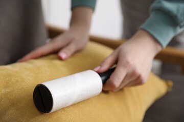 Fototapeta premium Woman cleaning pillow with lint roller at home, closeup