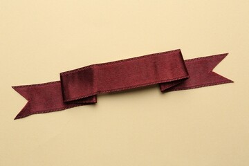 Burgundy ribbon on beige background, top view