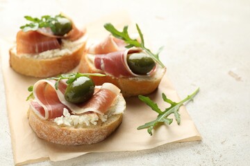 Delicious bruschettas with cream cheese, prosciutto, green olives and arugula on gray textured table, closeup. Space for text