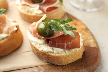 Delicious bruschettas with cream cheese, prosciutto, green olives and arugula on table, closeup