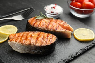 Tasty grilled salmon steaks served with lemon on black table, closeup