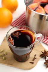 Mug with tasty mulled wine and ingredients on white wooden table, closeup