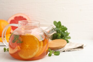 Aromatic fruit tea in glass teapot, orange, grapefruit and mint on white table, closeup. Space for text