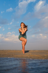 Woman performs Eagle Pose on beach at sunset while showing strength and focus