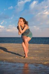 Woman performs Garudasana on sandy beach during sunset near the ocean waves