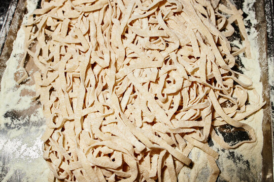 Fresh homemade pasta dough cut into long strips resting on floured surface, uncooked noodles arranged in pile showing texture and preparation process for traditional meal