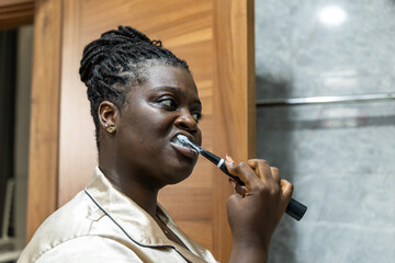 Young African woman in silk pajamas brushes her teeth in the bathroom