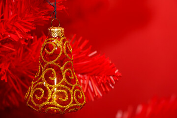 Bell ornament hangs on red Christmas tree branches during holiday season