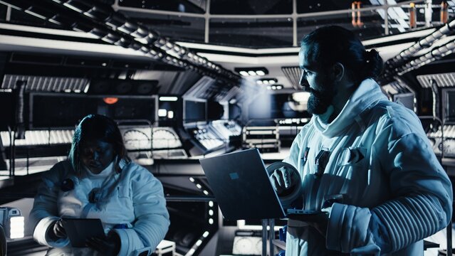 Astronaut studying star charts on laptop, discussing with colleague during space mission. Teamworking cosmonauts look at galaxy visualization on notebook during mankind survival expedition - Powered by Adobe