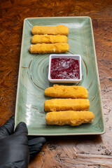 Crispy Fried Breaded Cheese Sticks with Red Dipping Sauce Served on Green Rectangular Plate over Rustic Wooden Background