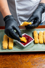 Chef Hands Wearing Black Gloves Breaking Fried Mozzarella Cheese Stick to Show Melted Texture Over Green Plate and Red Sauce