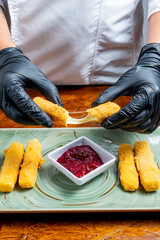 Chef Hands Wearing Black Gloves Breaking Fried Mozzarella Cheese Stick to Show Melted Texture Over Green Plate and Red Sauce
