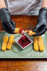 Chef Hands Wearing Black Gloves Breaking Fried Mozzarella Cheese Stick to Show Melted Texture Over Green Plate and Red Sauce