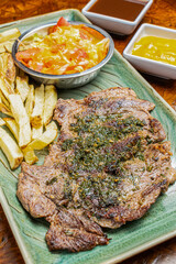 Top View of Grilled Beef Steak Topped with Green Chimichurri Sauce Served with Crispy French Fries and Fresh Tomato Salad