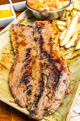Juicy Grilled Beef Steak with Sear Marks Served with French Fries and Fresh Salad on Rustic Ceramic Plate
