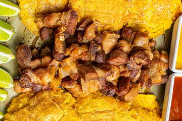 Traditional Colombian Chicharr&oacute;n with Fried Plantains, Lime and Dipping Sauces, Crispy Pork Belly Close Up