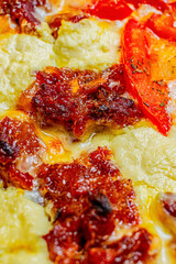 Close-up of a slice of pizza with caramelized bacon, mango, and cream cheese on a mixture of melted cheeses.