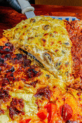 Chef lifts a slice of chicken and mushroom pizza using a spatula from among several varieties of pizza on parchment paper.