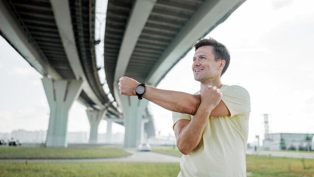 Man stretches underneath a large bridge in the city