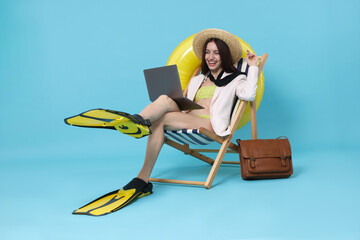 Businesswoman with laptop and flippers in deck chair on light blue background © New Africa