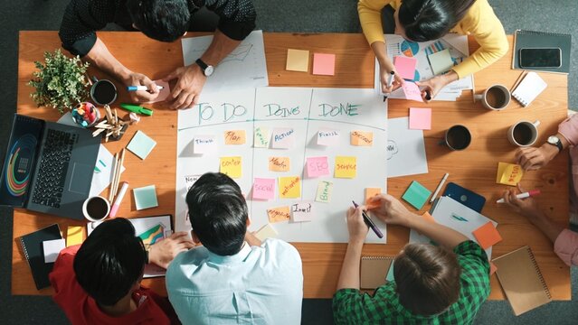 Top down aerial view of diverse business team making scrum task board at meeting room. Group of smart people writing at paper and sticky notes for making kanban board to manage work flow. Convocation.