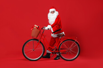 Santa Claus with bicycle and Christmas gifts in basket on red background