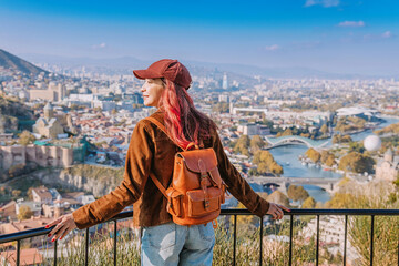 Woman with backpack admiring the panoramic cityscape of Tbilisi, Georgia, from a high viewpoint, experiencing travel and tourism © EdNurg