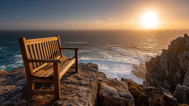 An empty wooden bench rests on a rocky clifftop overlooking the expansive ocean during a golden hour sunset. - Powered by Adobe