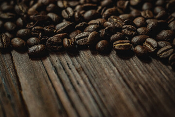 Fototapeta premium Roasted coffee beans scattered on a rustic dark wooden table, creating a rich brown texture and background for morning concepts