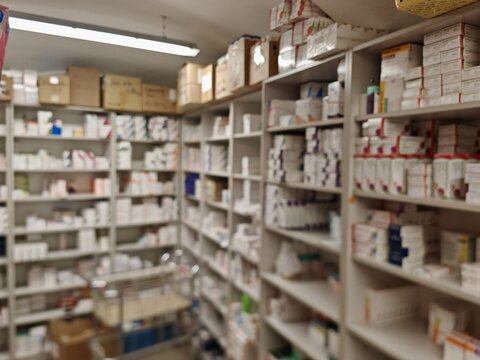 Blurred view of a pharmacy warehouse filled with stocked boxes of medicinal products and vitamins, illustrating pharmaceutical supply chain, inventory management, and healthcare distribution system