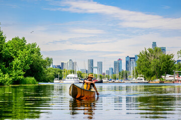 Solo canoeist paddles near the Toronto skyline on the Toronto Islands, blending urban waterfront views with quiet summer recreation on calm freshwater.