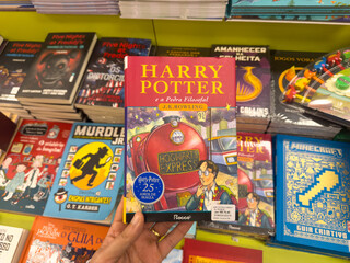 Naklejka premium BELO HORIZONTE, MG, BRAZIL, DECEMBER 12, 2025 Hand holding a special edition of Harry Potter and the Philosopher's Stone in a bustling bookstore, celebrating 25 years of magic.