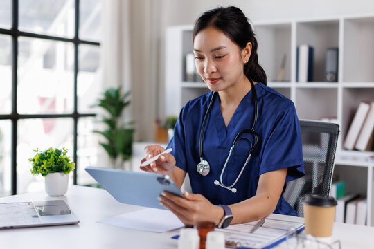 An attractive and professional Asian female doctor with blue coat or Asian female doctor working on her medical cases at her desk in the office at a hospital.
