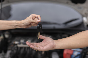 Close-up of hands exchanging car key in front of an open hood, symbolizing car rental, repair, handover, or sale. Perfect for automotive services, car dealership and roadside assistance concepts.