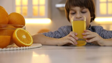 Boy jumping from under table and drinking fresh orange juice in kitchen