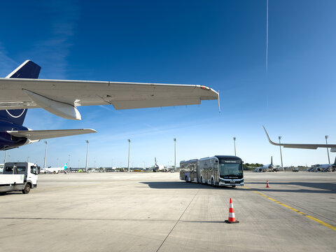MUNICH, GERMANY - JUNE 21, 2025: Airport apron bus drives across the tarmac at Munich International Airport. Airside scene with aircraft wings, and ground handling area, on passenger transfer.
