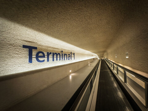 PARIS, FRANCE - JUNE 21, 2025: Moving walkway inside Terminal 1 at Paris Charles de Gaulle Airport, long concrete corridor and accent lighting guiding passengers. Paris CDG is paris' main airport.